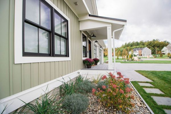 Exterior view of a house with sage green siding, black window trim, porch, and landscaped yard.