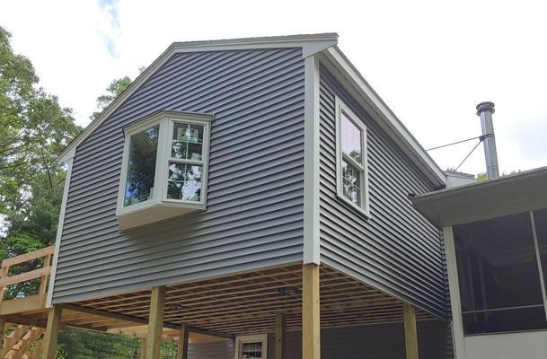 Elevated gray house with bay window, wooden deck, and white trim.