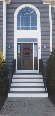 Gray house with arched window, front door, steps, and a wreath.
