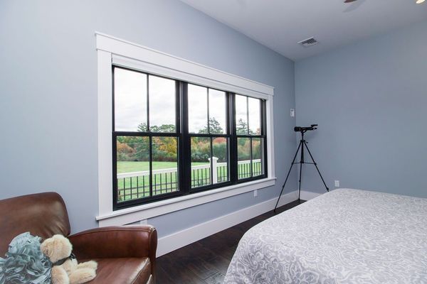 Bedroom with a large black-framed window and a telescope. Brown leather chair, blue walls, and a bed.