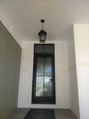 Black framed door with glass panels, lantern, white paneling, and gray siding.