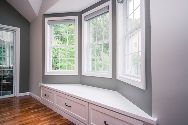 Bay window with a white bench, gray walls, and three windows with a lush green view.