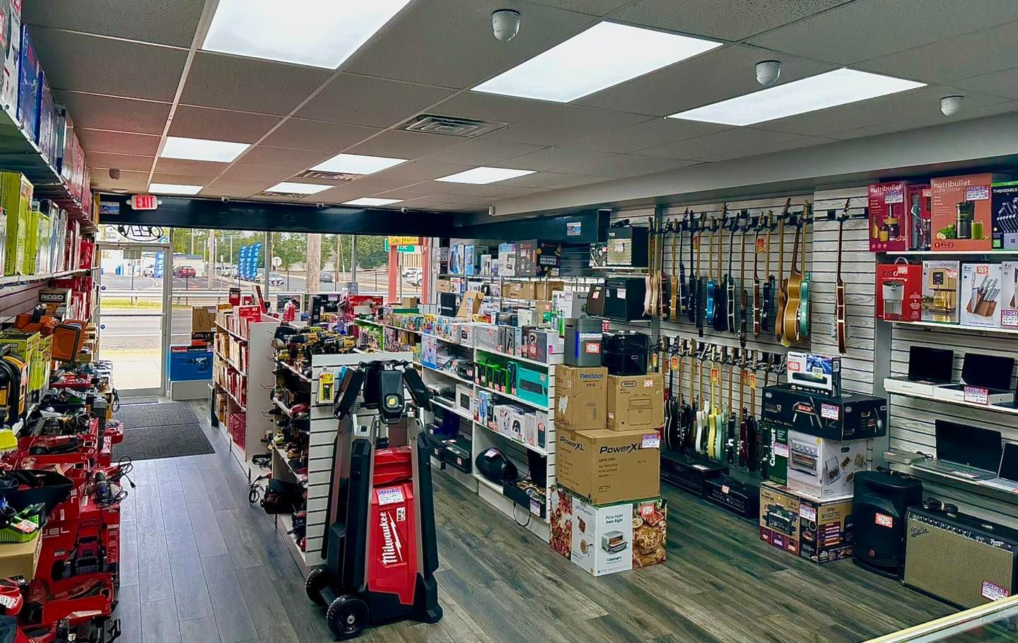 Interior of an electronics store with various products on shelves and guitars hanging on the wall.