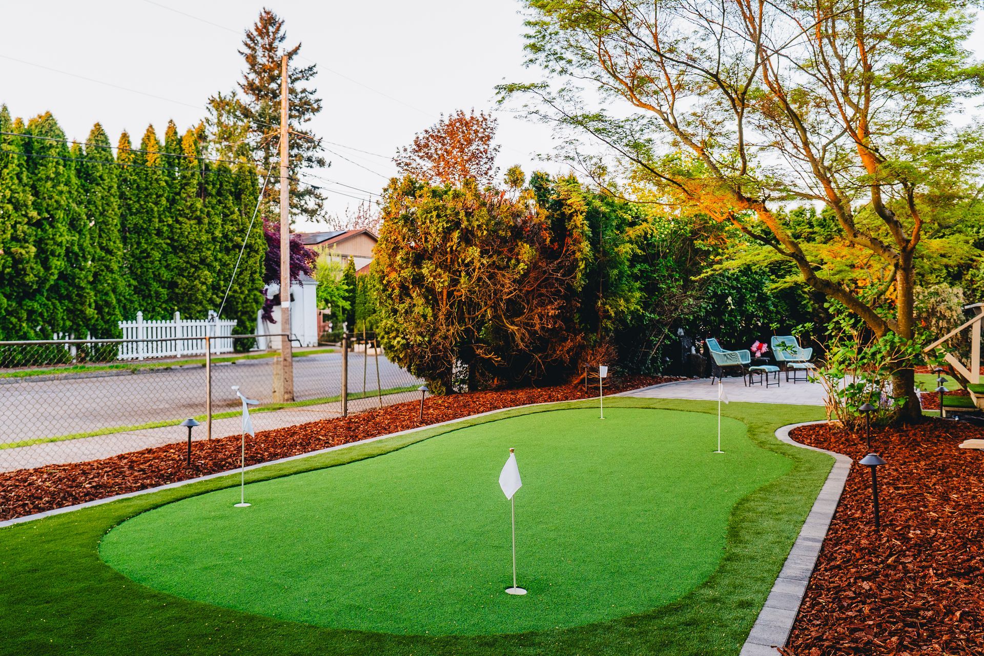 Miniature golf green with white flags, surrounded by landscaping and trees.