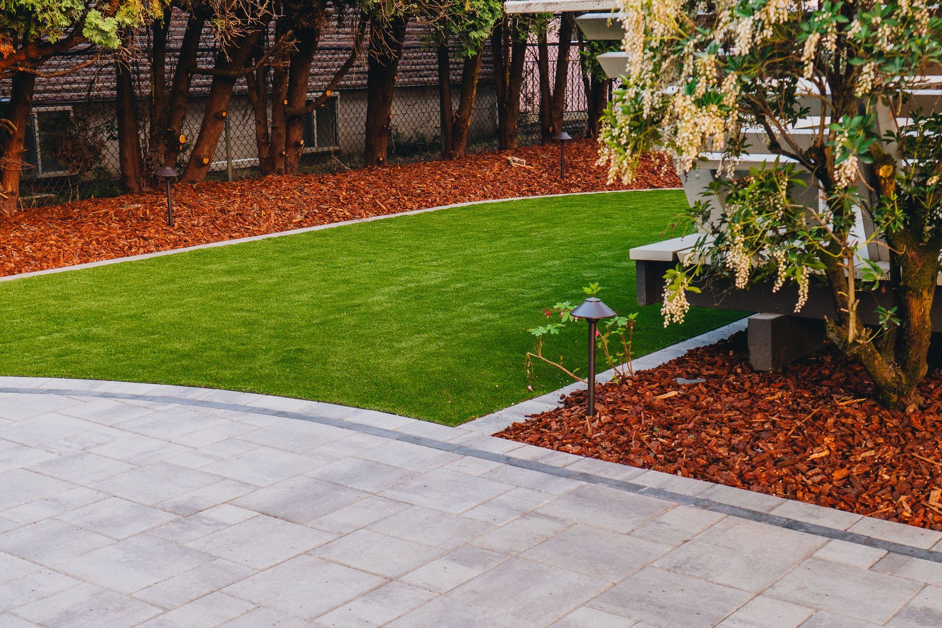 Backyard with a gray stone patio, green lawn, brown mulch, and trees.