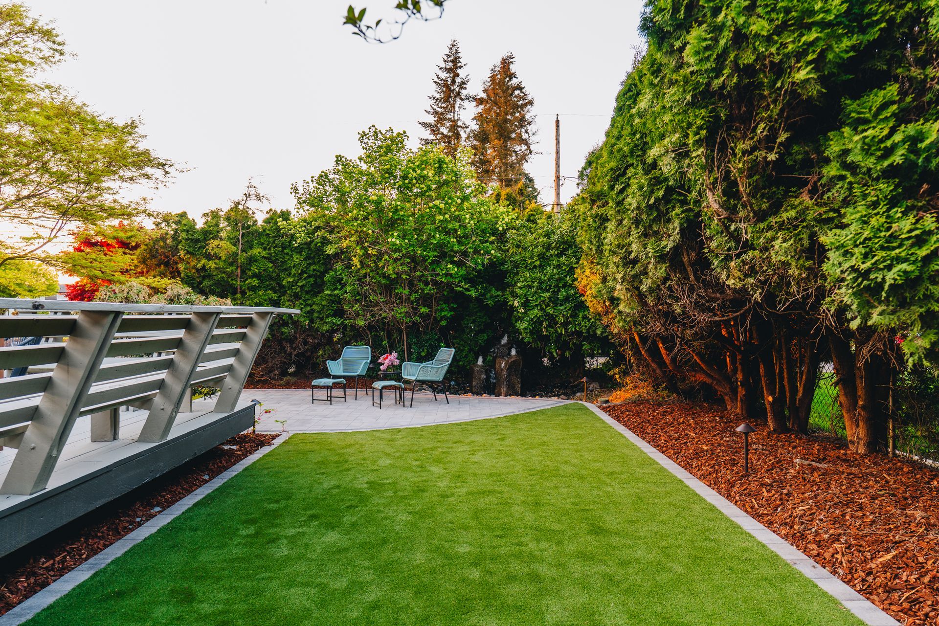 A backyard patio with artificial turf and seating surrounded by trees.