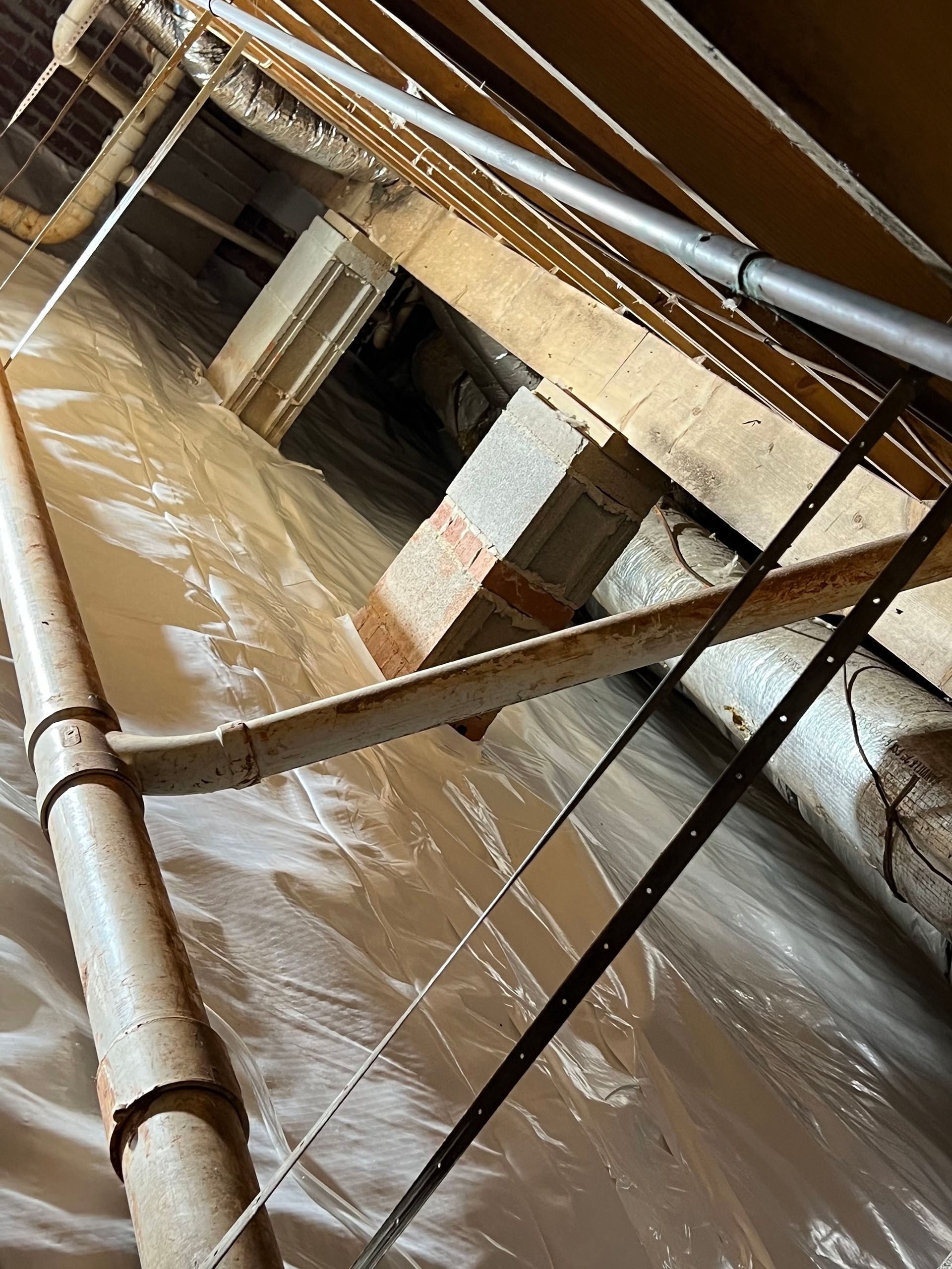 Crawl space with insulation, pipes, brick support, and wood beams.