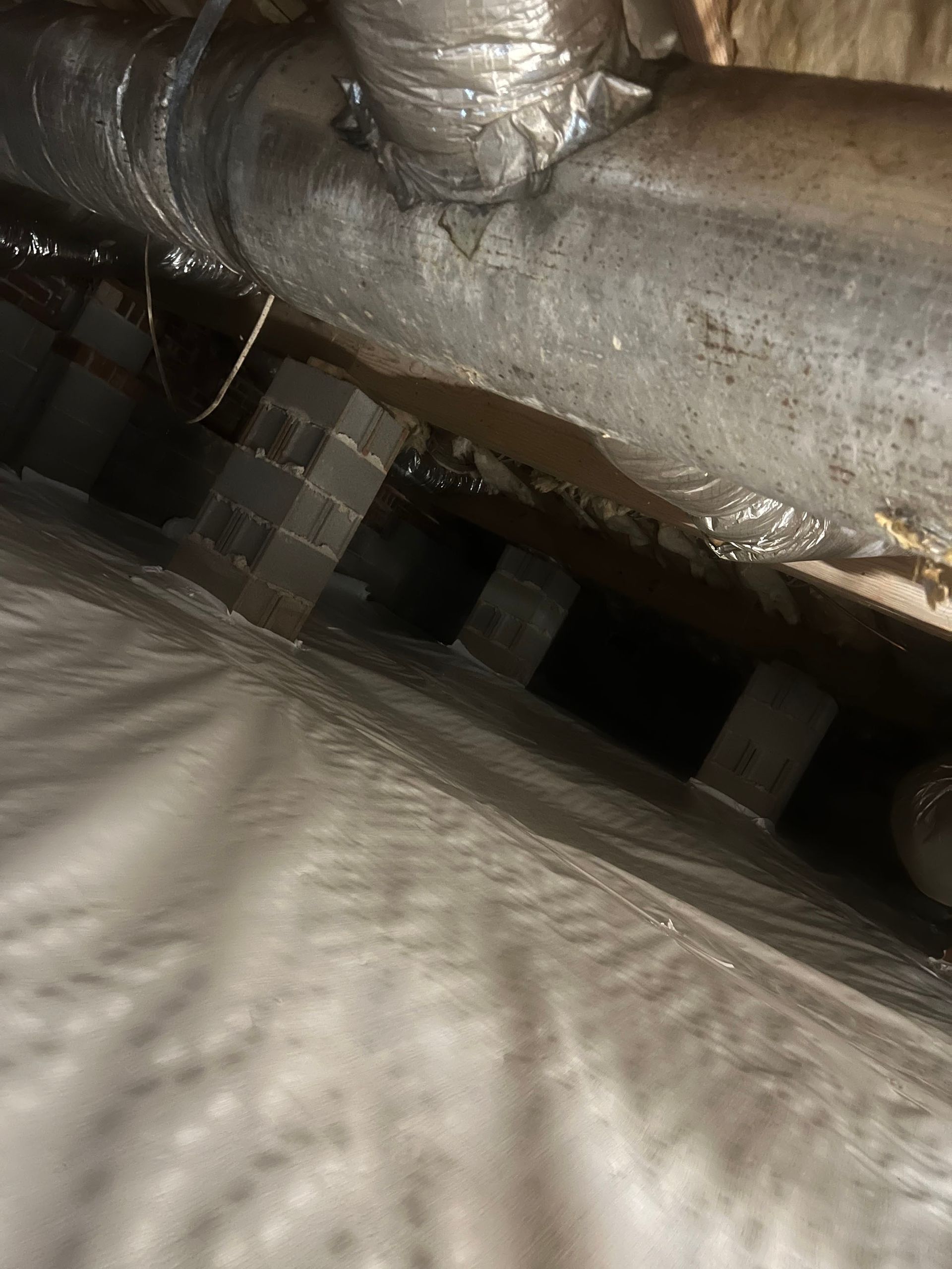 A crawlspace with ductwork above supported by brick stacks. Gray insulation and water are visible.