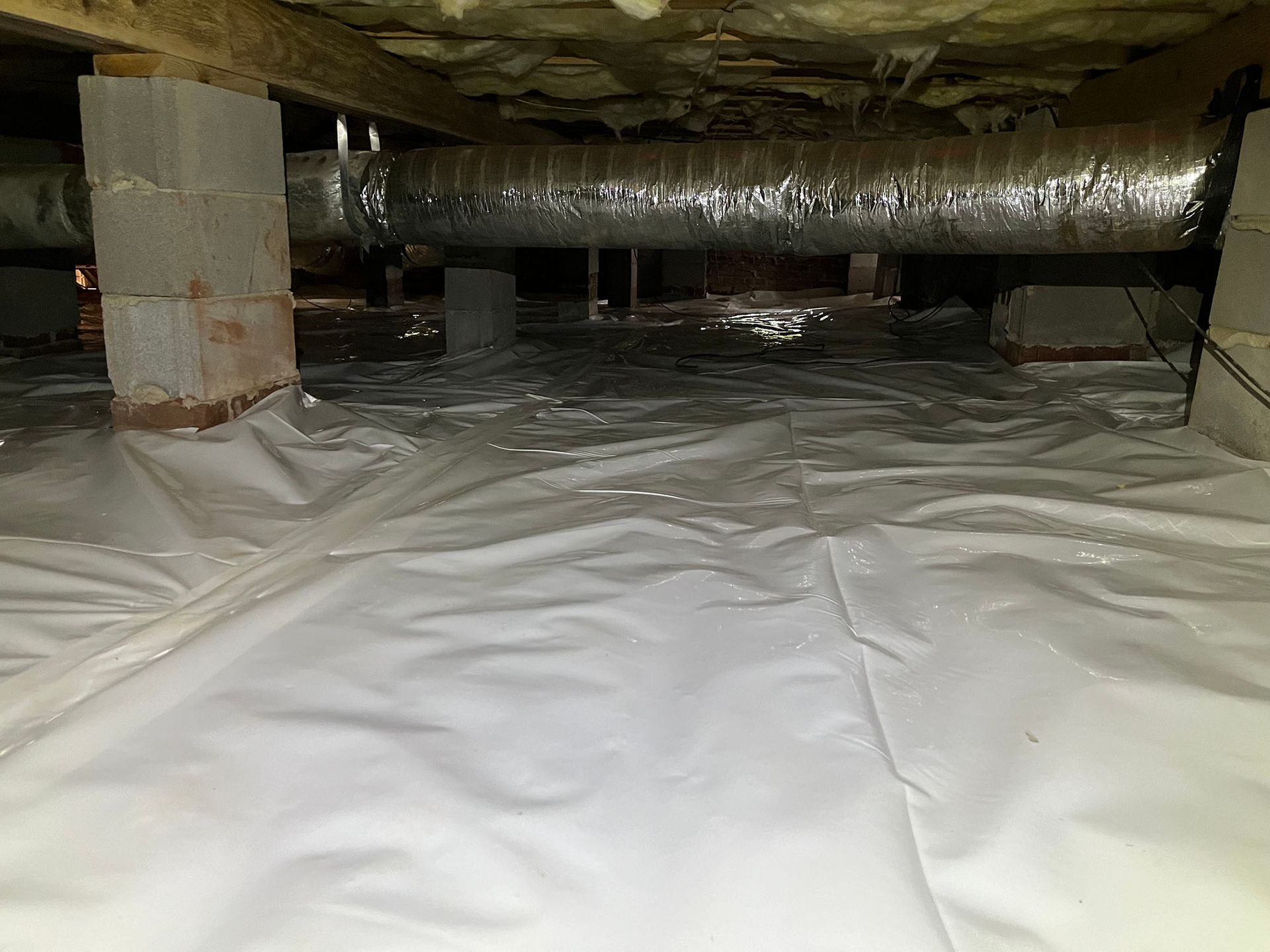Crawlspace with white plastic vapor barrier covering the ground. Air ducts and concrete supports are visible.