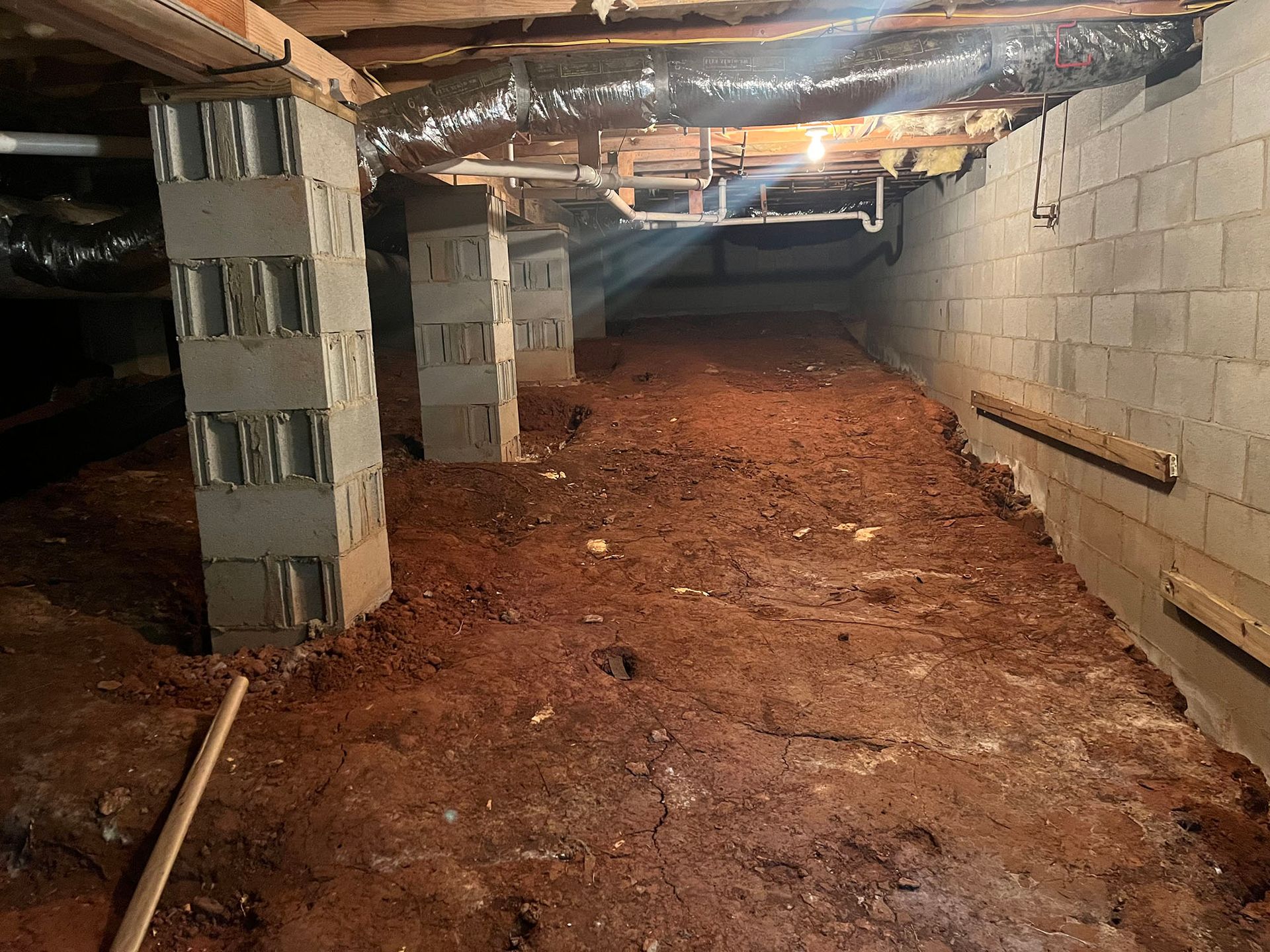 Crawlspace with cinder block pillars, dirt floor, and visible pipes.