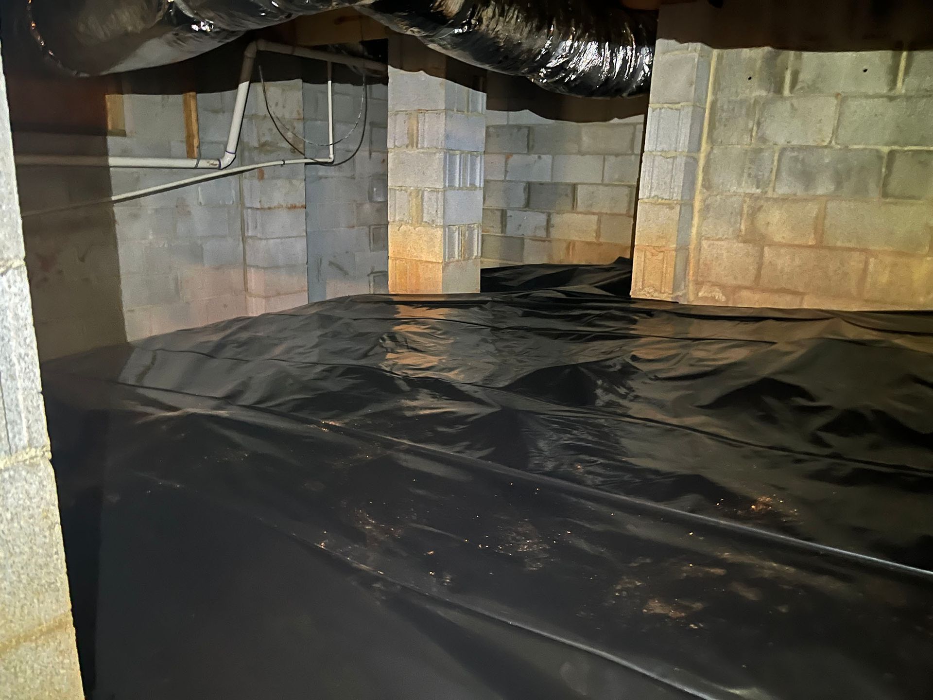 Black plastic sheeting covering the ground in a crawl space, against concrete block walls.