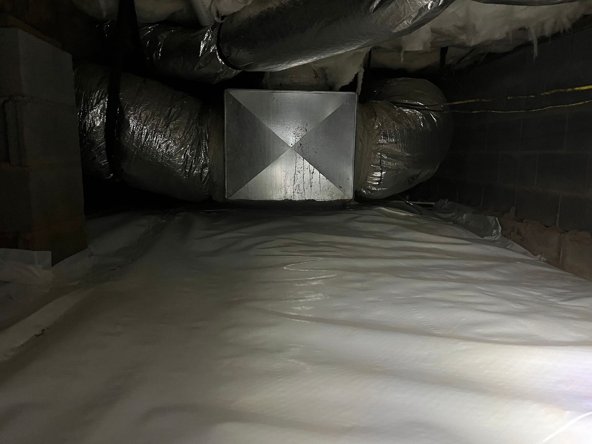 Crawlspace with white vapor barrier, metal ductwork, and insulation.