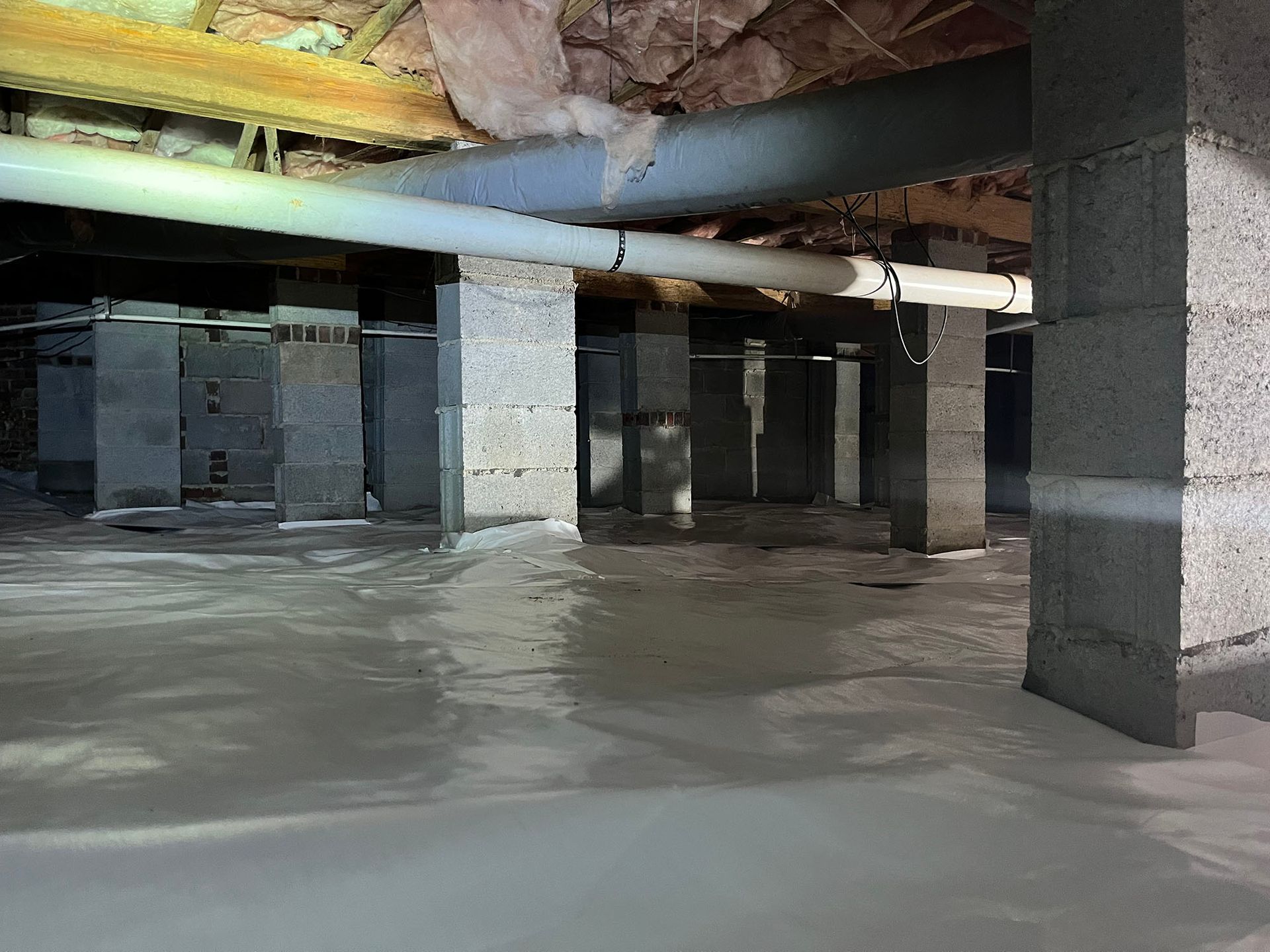 A crawl space with concrete block supports and a white, reflective floor. Ductwork and beams are visible overhead.