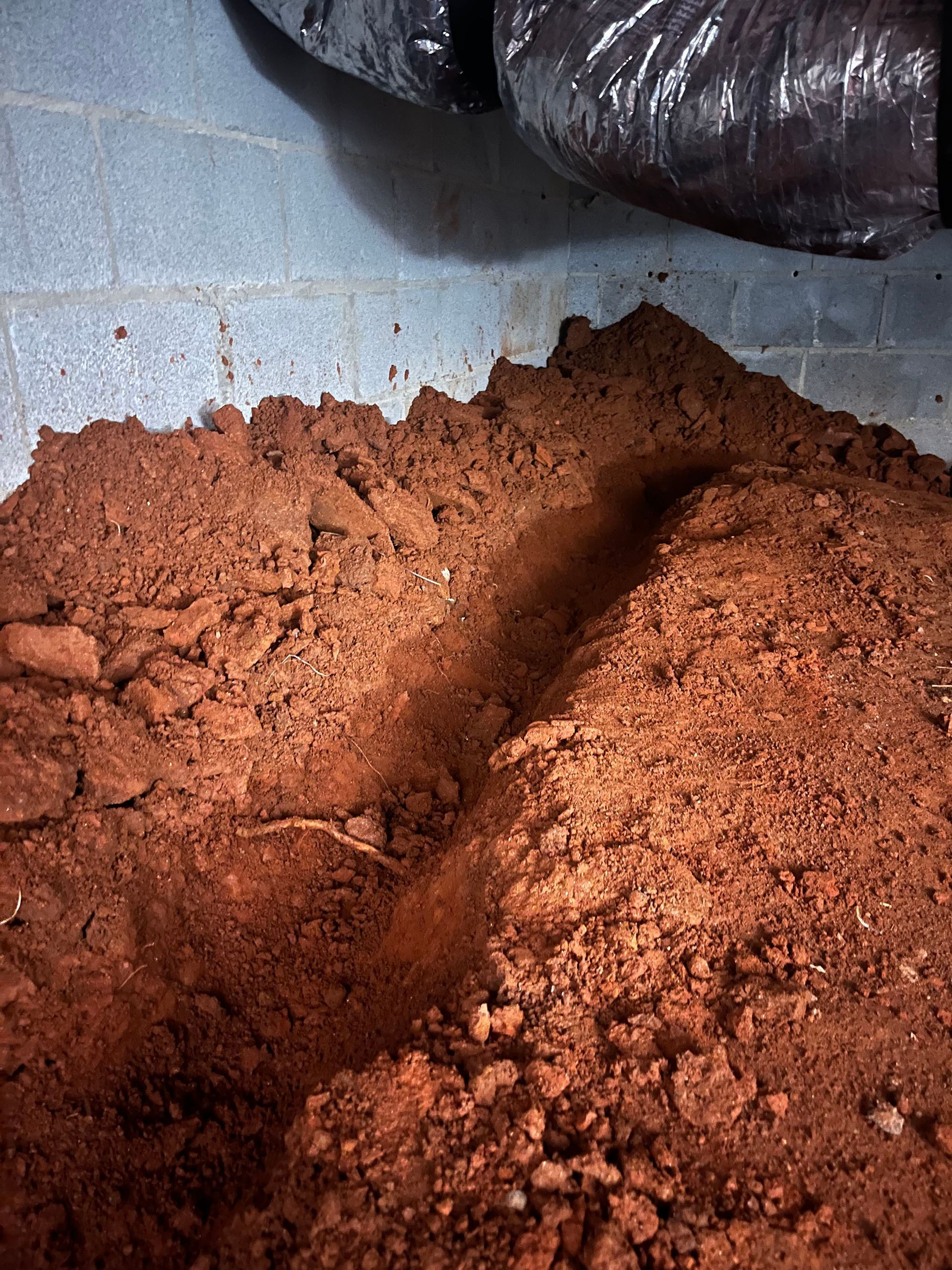 Pile of reddish-brown dirt against a gray concrete wall, with black HVAC ductwork above.