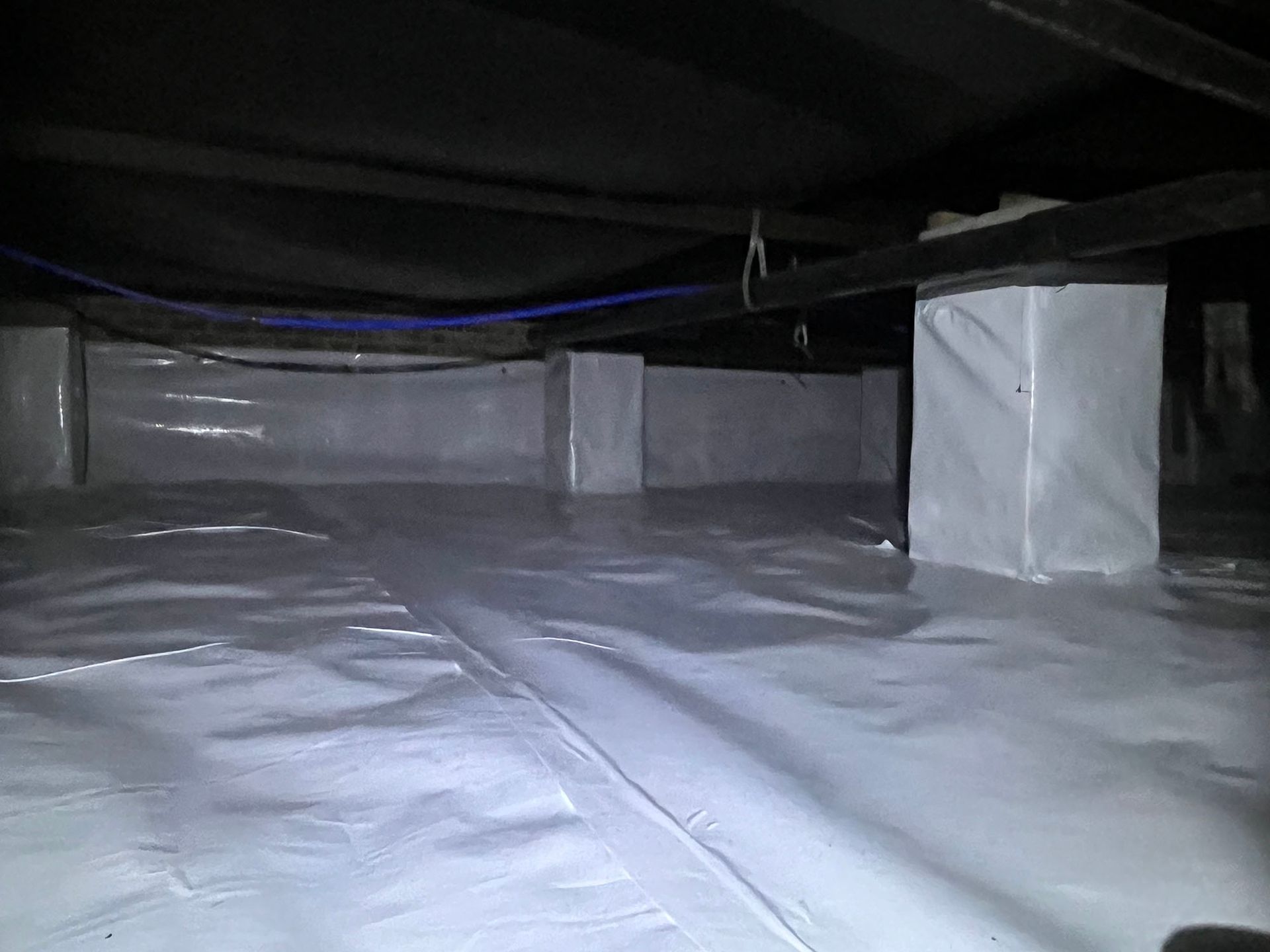 White crawl space with vapor barrier on floor, insulation around support columns.
