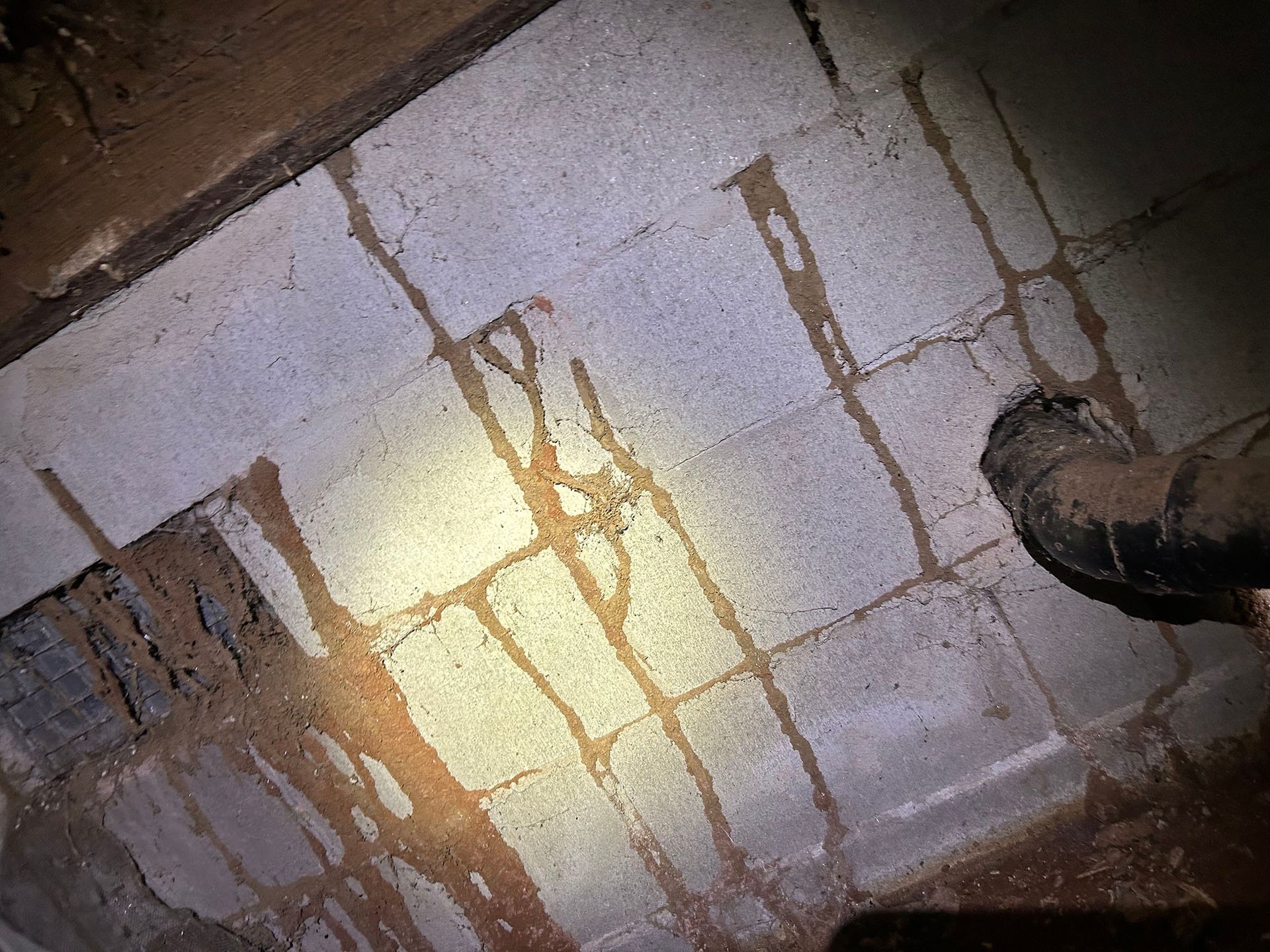 Termite mud tubes on concrete block foundation. Brown streaks. Dark corner with pipe.