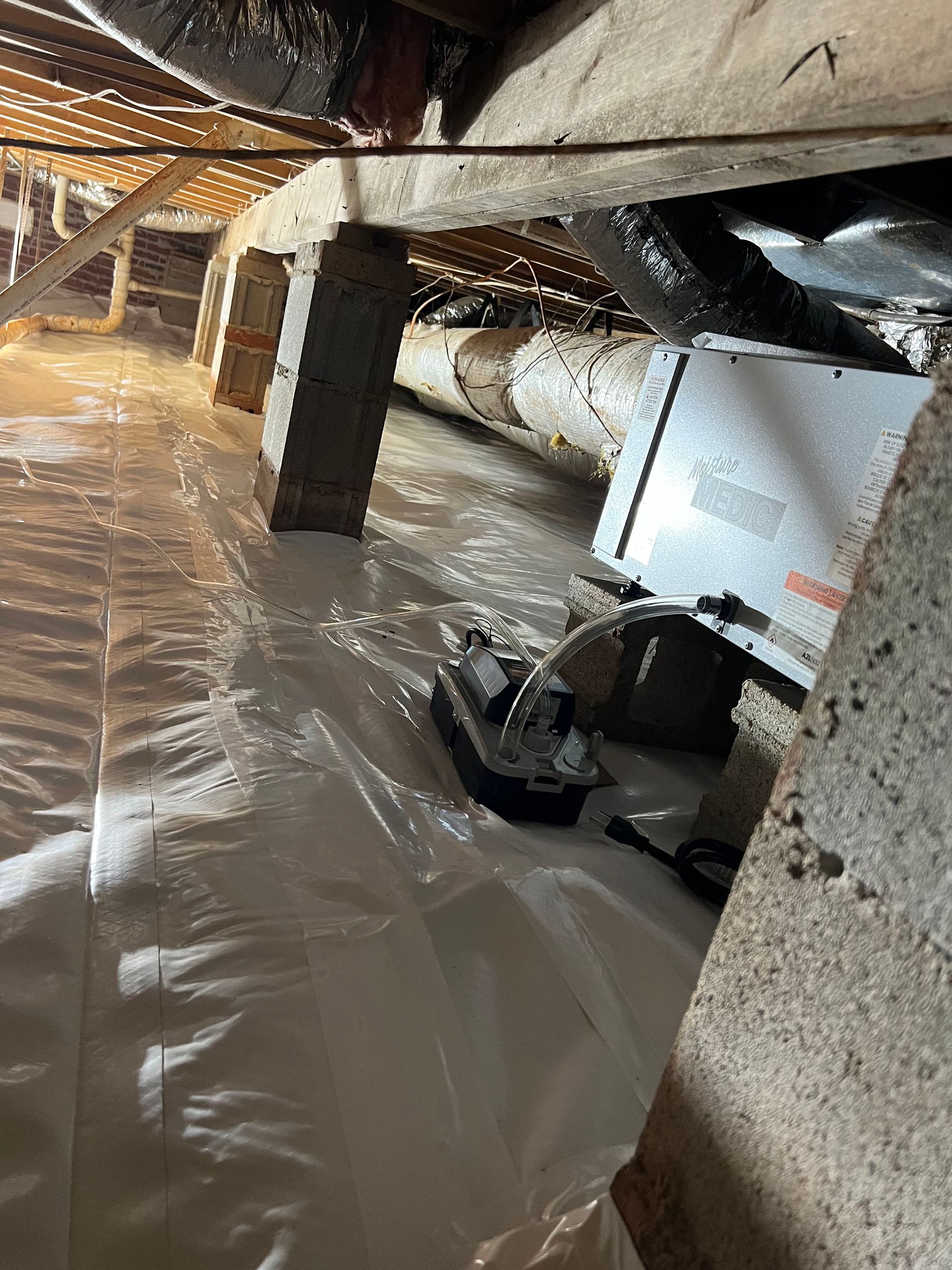 Crawl space with white vapor barrier, wooden beams, HVAC unit, and ductwork.