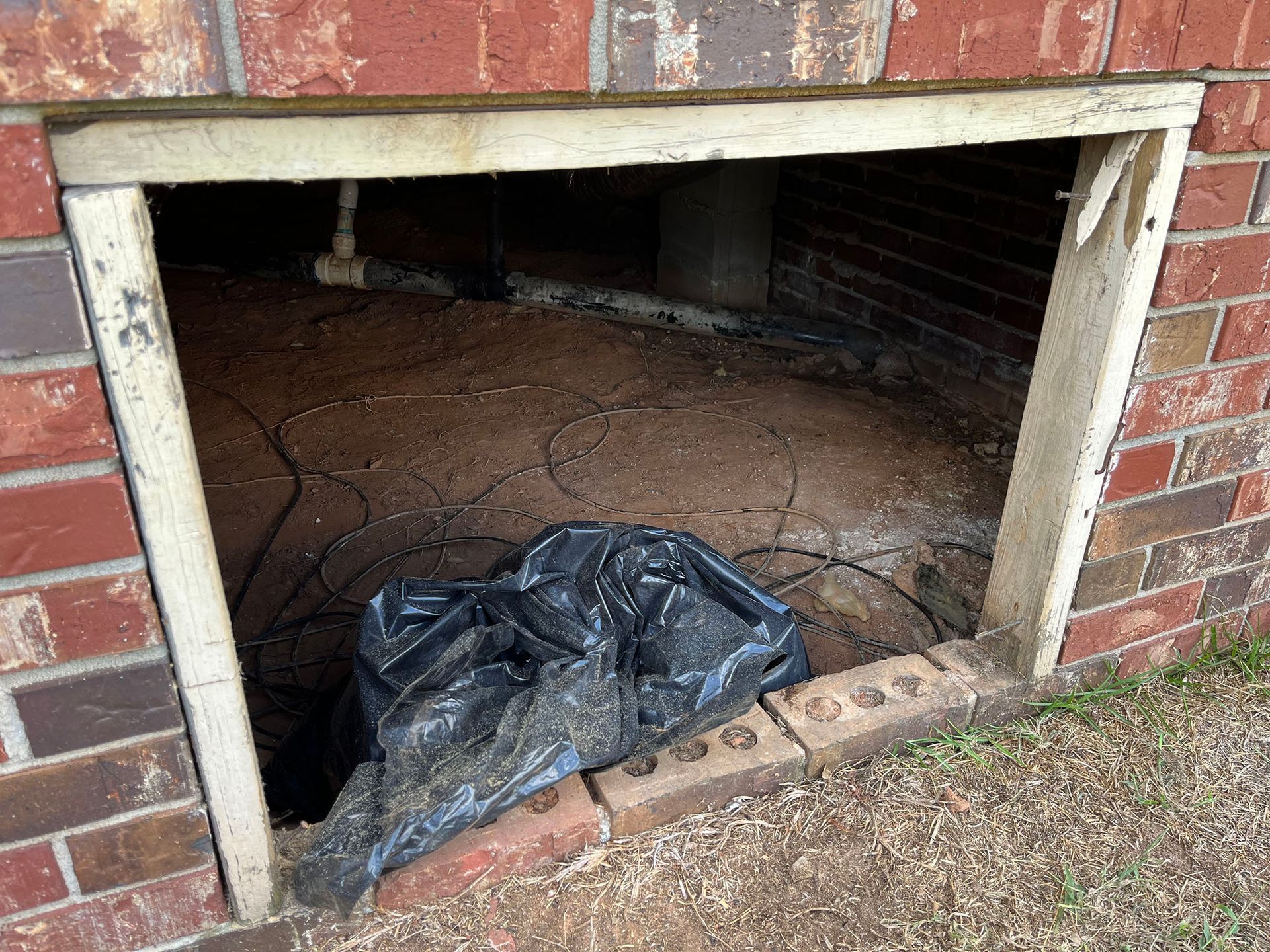 Opening in brick wall with trash bag inside; wooden frame around the opening.