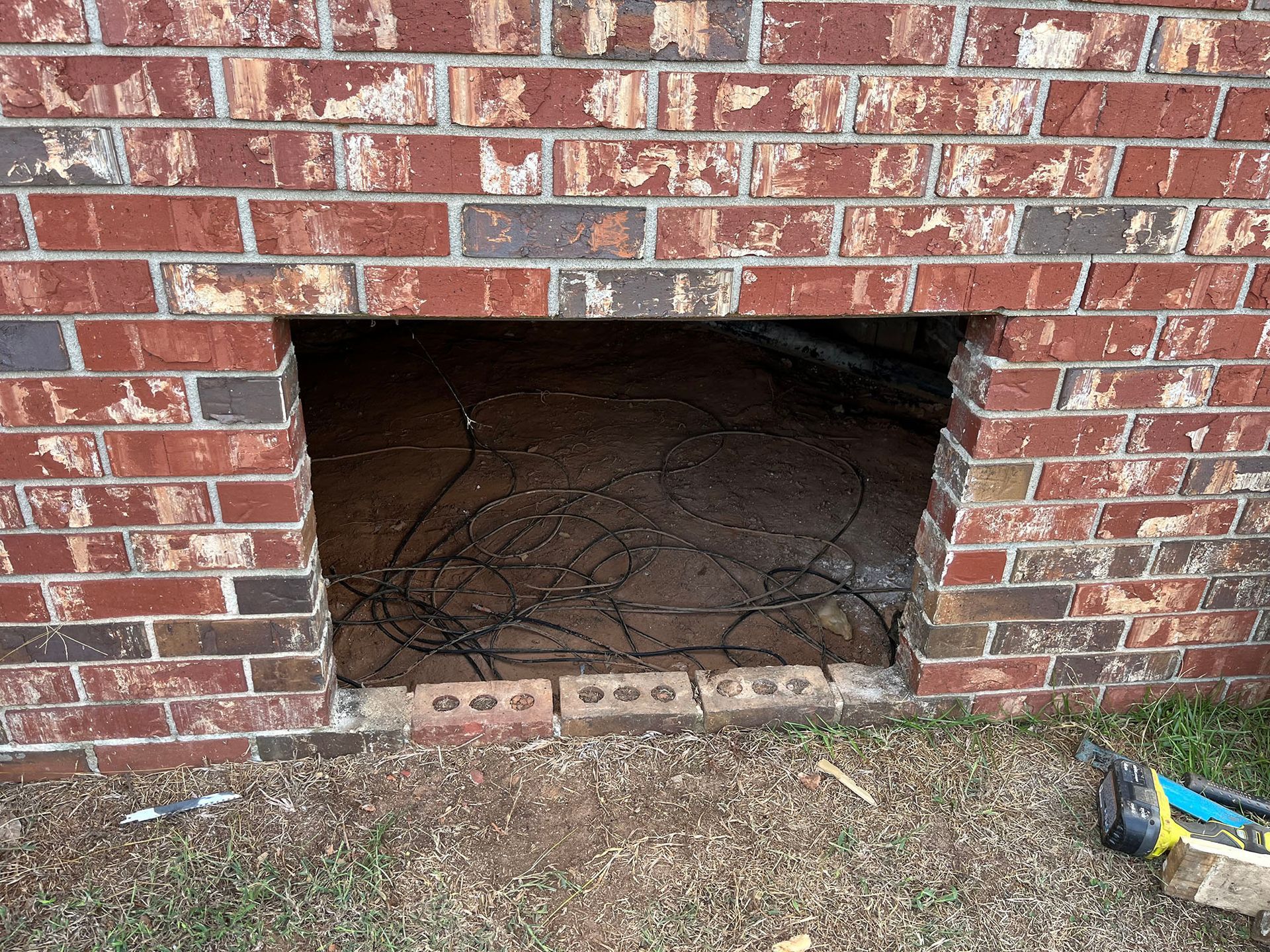 Brick wall with rectangular opening containing wires. Ground level, exterior.