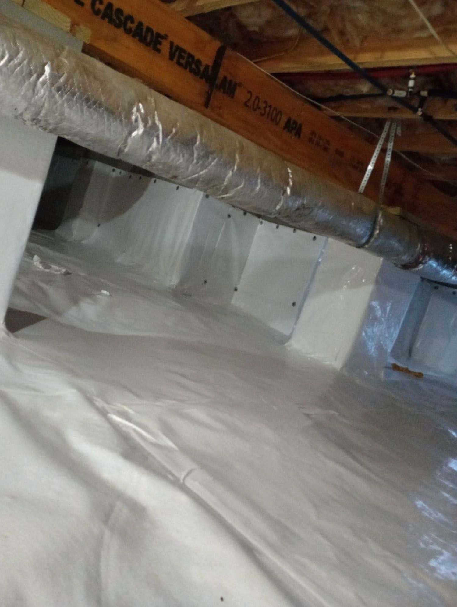 Crawl space with white vapor barrier covering the ground and walls, ductwork overhead.