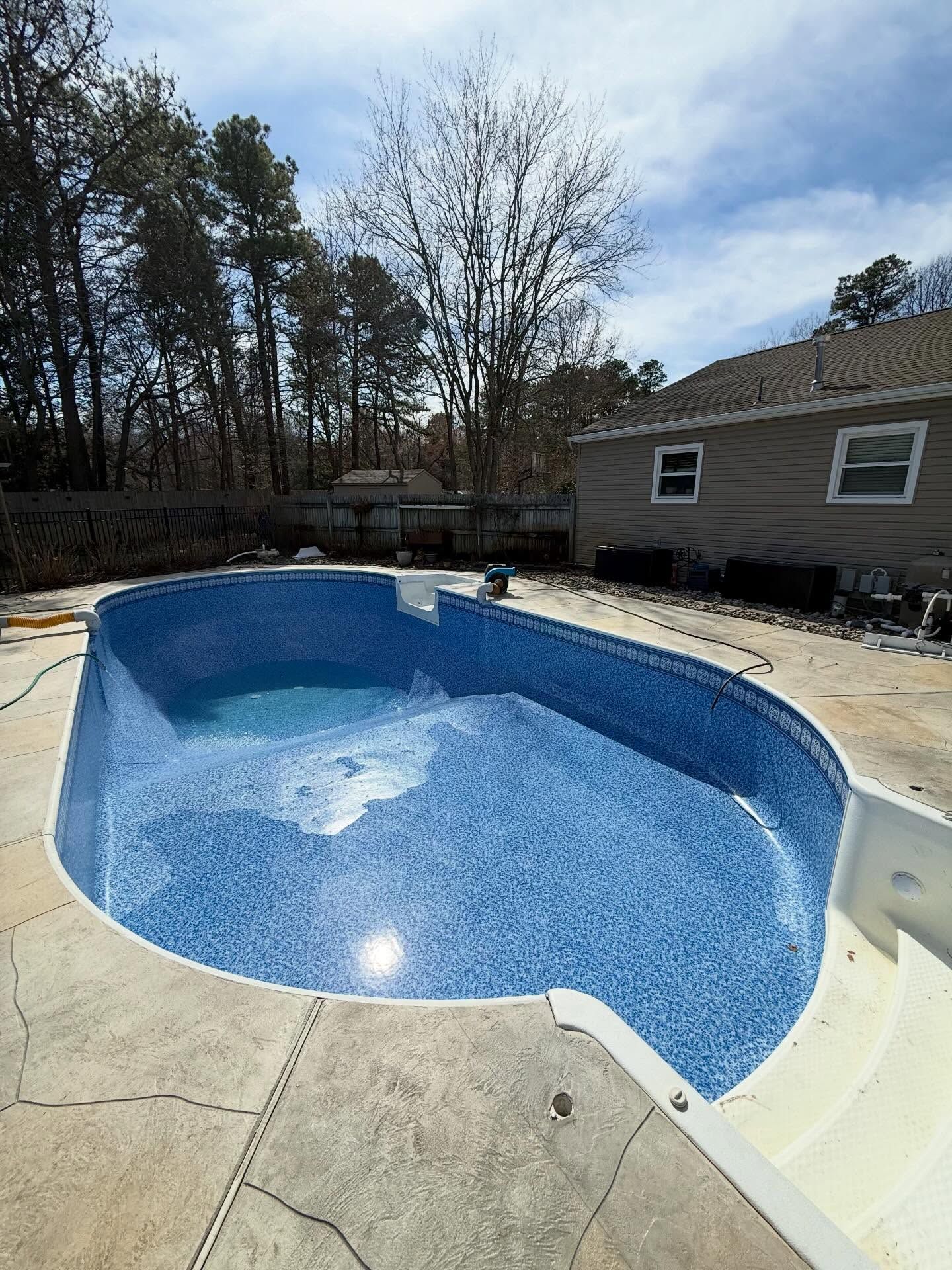 Empty in-ground pool with blue water and white coping beside a house and trees