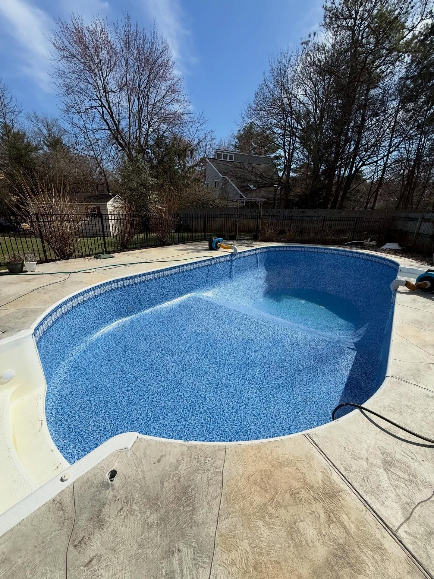 Empty blue backyard swimming pool with beige concrete deck and leafless trees around it