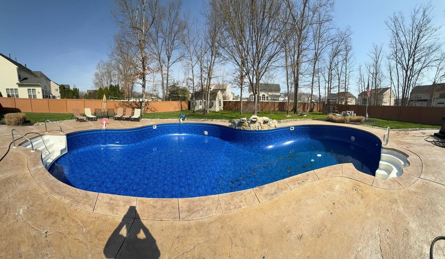 Backyard with a blue in-ground swimming pool under construction, surrounded by dirt and stone edging