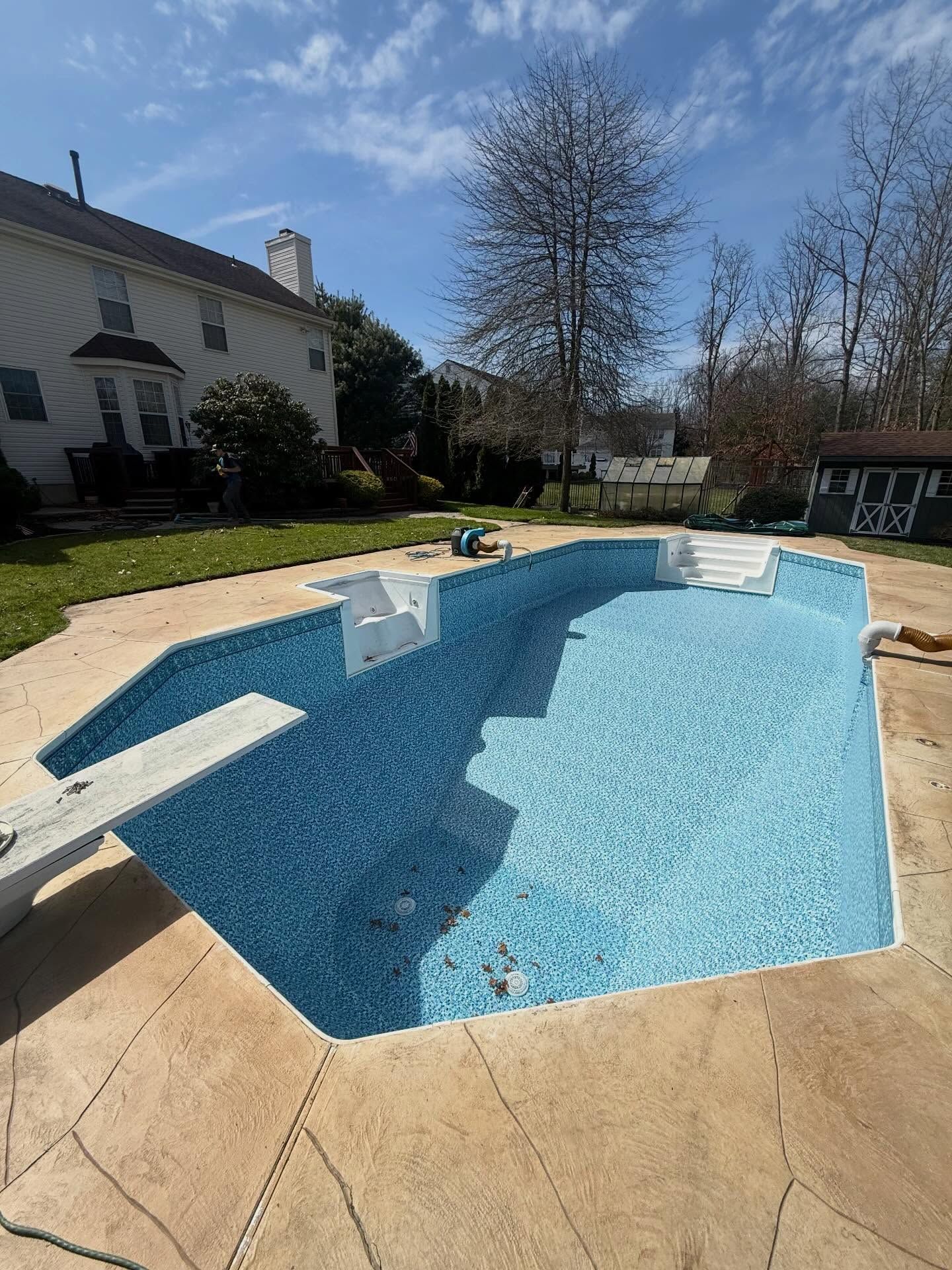 Empty backyard swimming pool with blue mosaic lining and beige patio under a clear sky