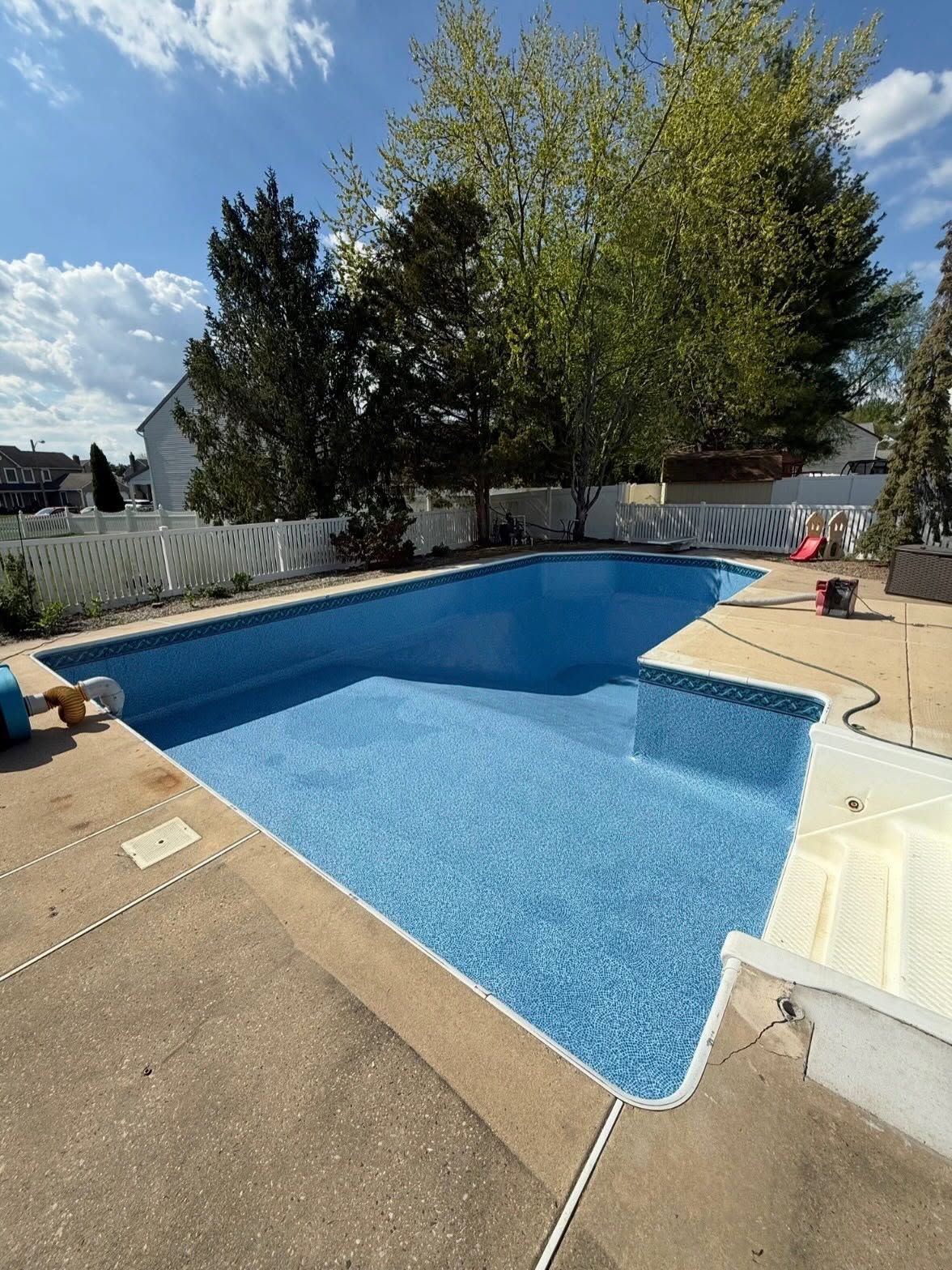 Backyard swimming pool with blue water, white steps, and trees in the background
