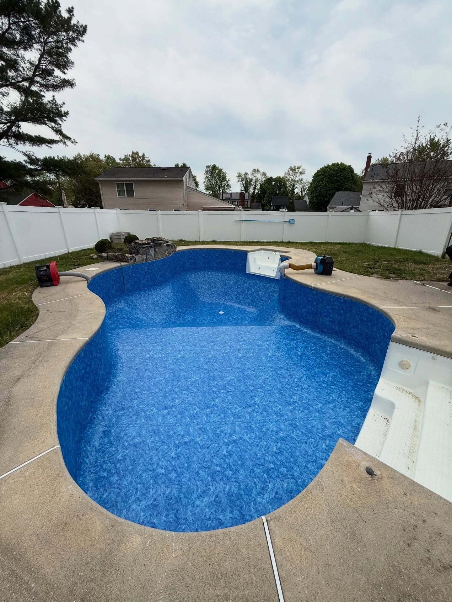 Empty blue in-ground swimming pool with white fencing and concrete deck in a backyard.