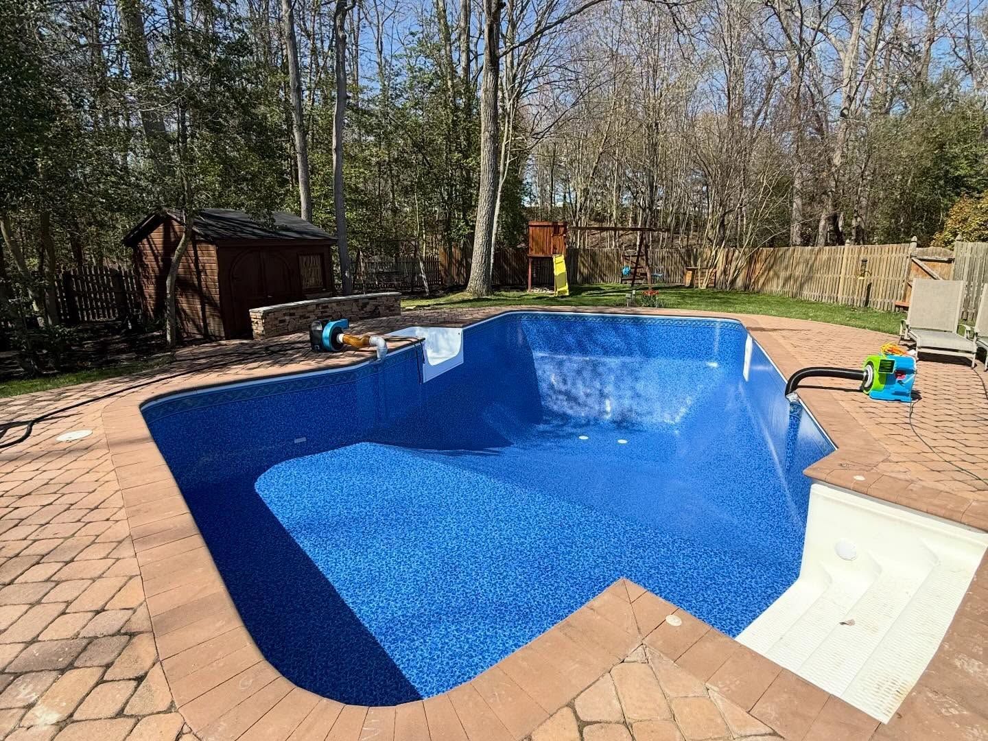 Blue in-ground swimming pool with patio, trees, and a small shed in the backyard