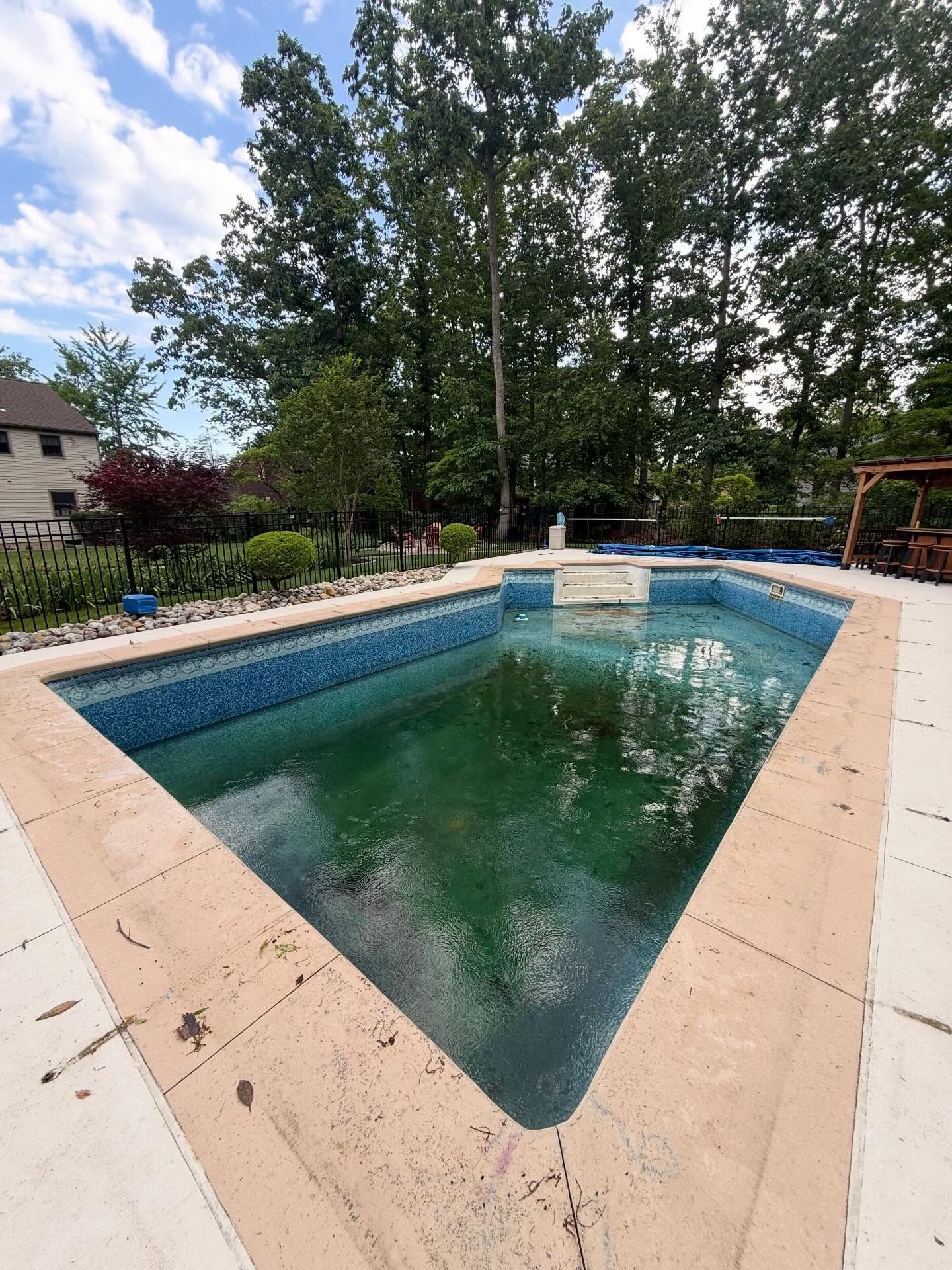 Backyard in-ground pool with turquoise water, beige deck, and trees around it