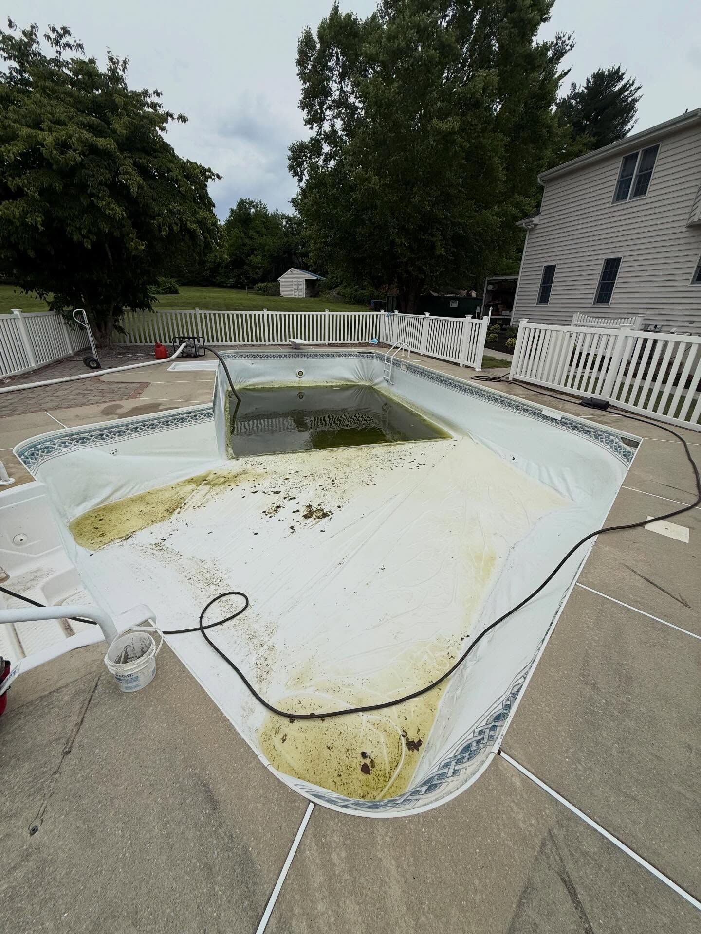 Empty in-ground swimming pool with stained white surface beside a house and patio railing.