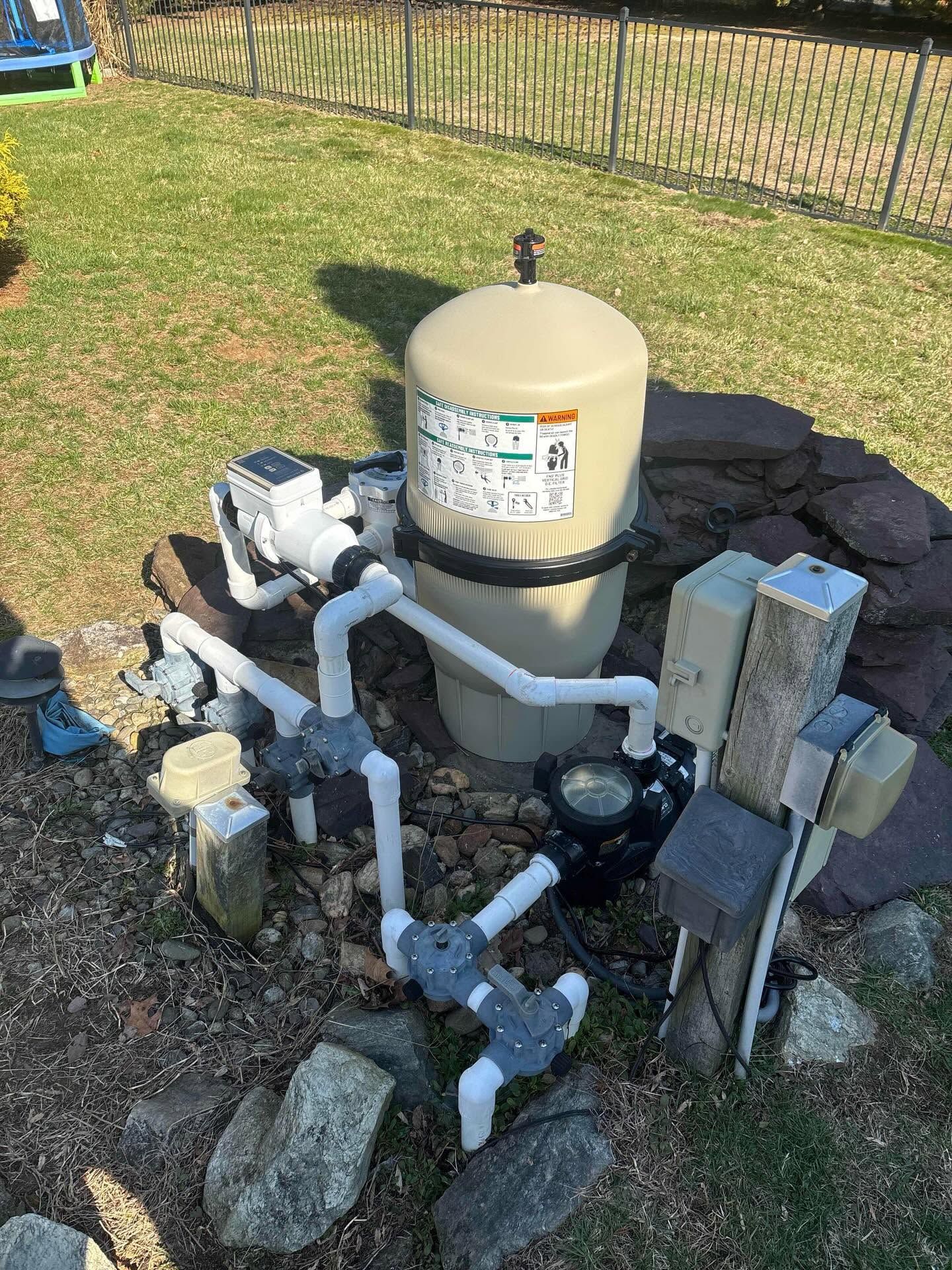 Pool filter and pump equipment with white PVC pipes beside a yard fence.