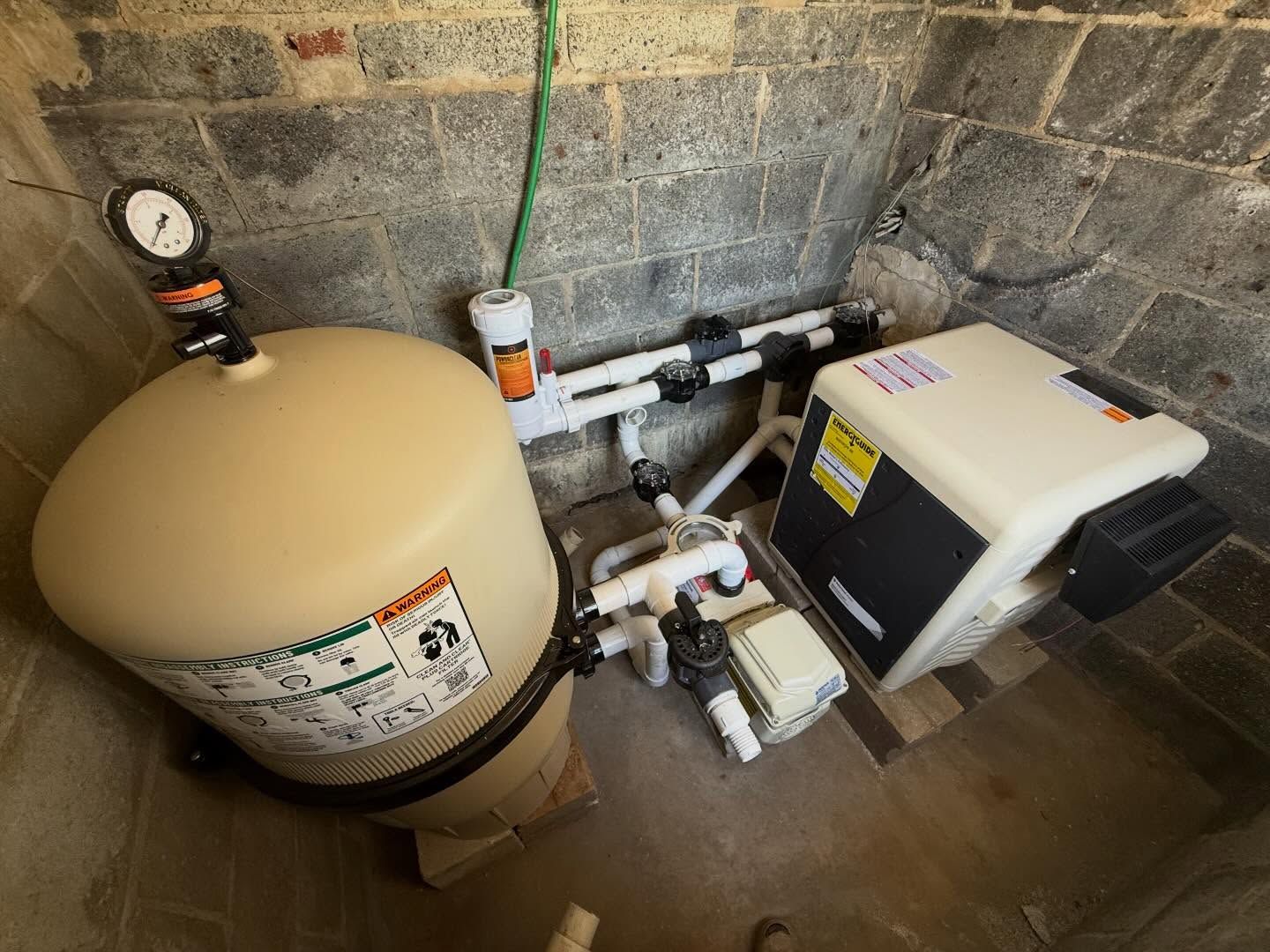 Water heater, pressure tank, and furnace in a utility room with concrete block walls.