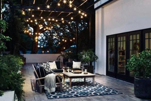A patio with a couch , chairs , and a table with lights hanging from the ceiling.
