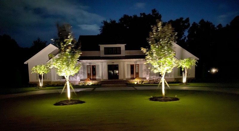 A house is lit up at night with trees in front of it.