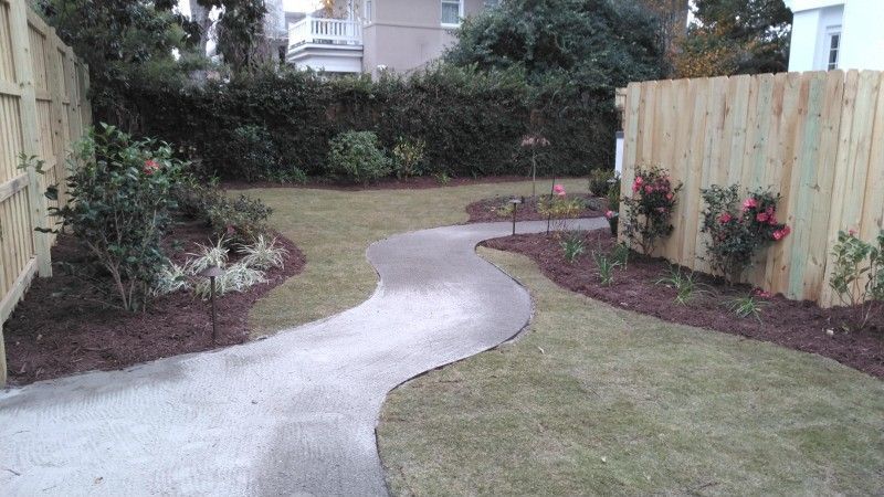 A concrete walkway leading to a wooden fence in a backyard.