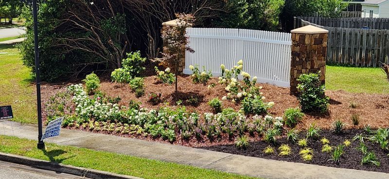 A white picket fence is surrounded by a lush green lawn and flowers.