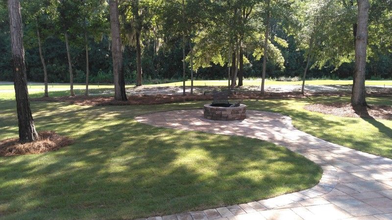 A fire pit in the middle of a lush green field surrounded by trees.