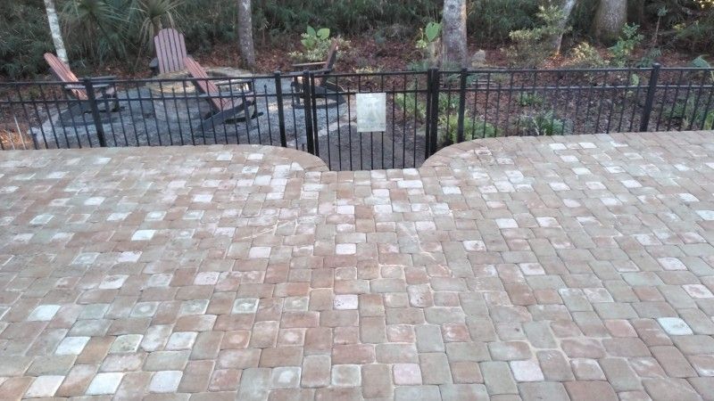 A brick patio with a metal fence and chairs in the background.
