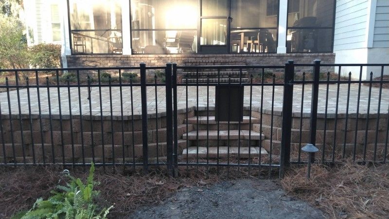 A black fence surrounds a screened in porch with stairs leading up to it.