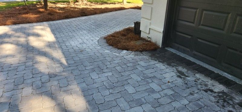 A brick driveway leading to a garage with a tree in the middle of it.