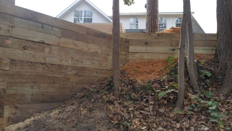 A wooden fence is surrounded by trees and dirt in front of a house.