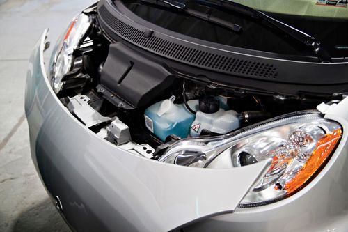 A close-up of a silver car's front hood popped open, revealing the engine compartment, headlights, and fluid reservoirs.