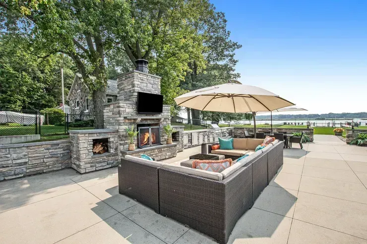 Patio with stone fireplace, outdoor seating, umbrella, and lake view.