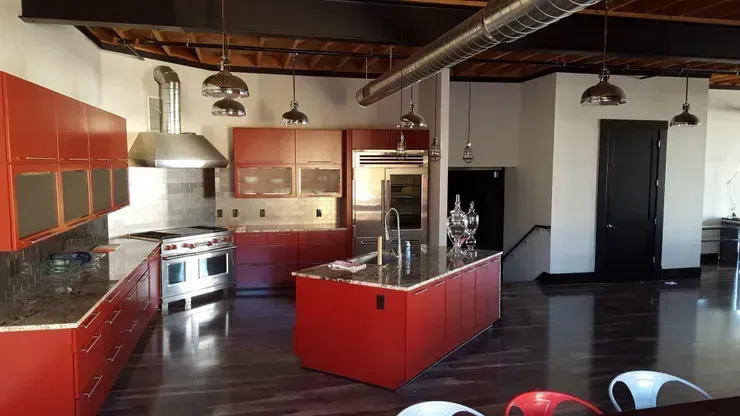 Red and stainless steel kitchen in an open-plan loft; red cabinetry, island, and appliances; black door, pendant lights.
