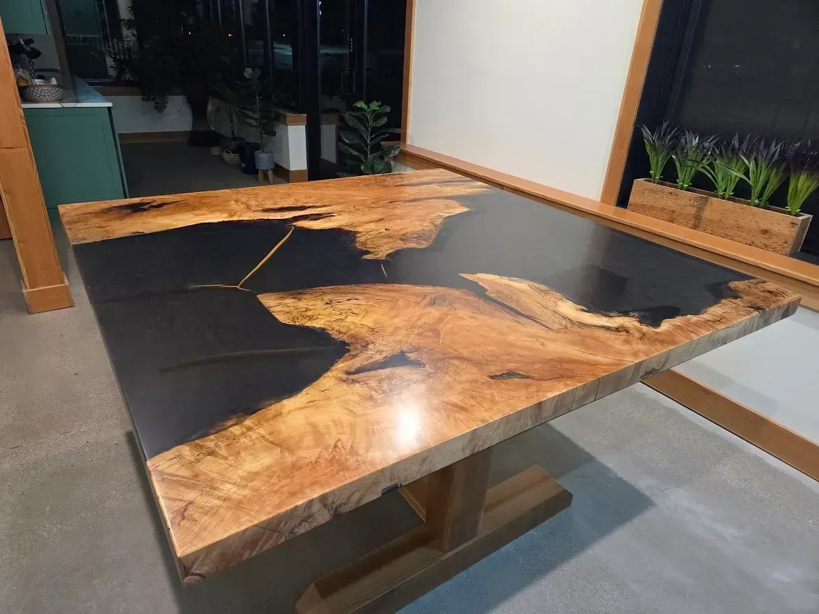 Square wooden table with dark glossy center and natural edge, light-colored wood, supported by a light-wood base.