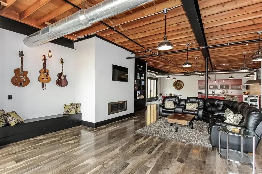 Loft interior with exposed ceiling, guitars on wall, black leather sectional, and hardwood floors.
