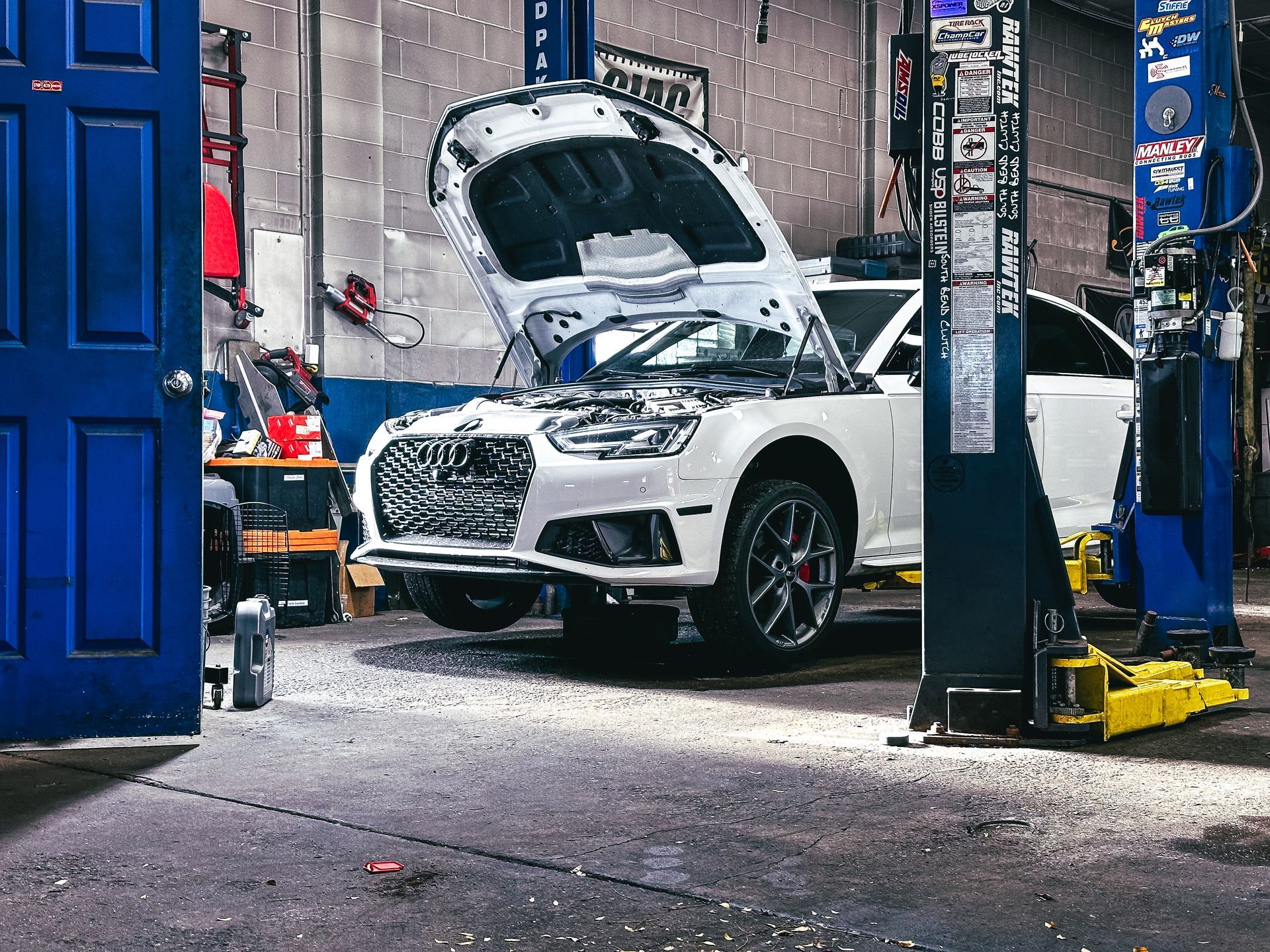 A white car with the hood up is sitting on a lift in a garage